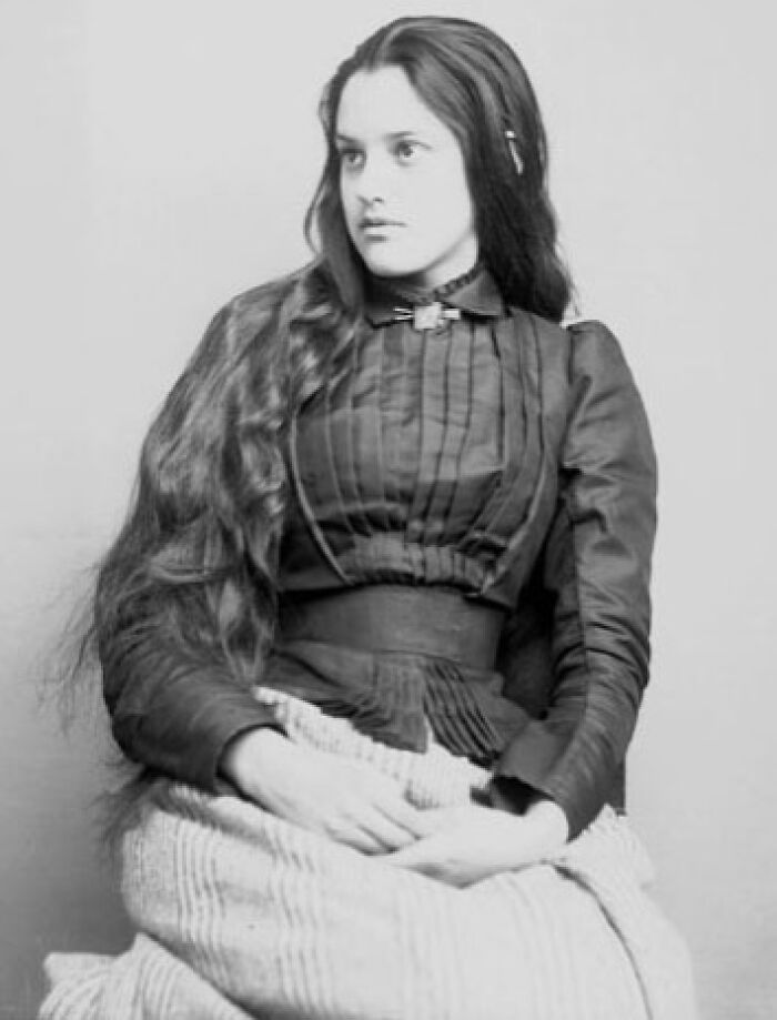 Native American woman in traditional attire with long hair, captured in a time-weathered black and white photograph.