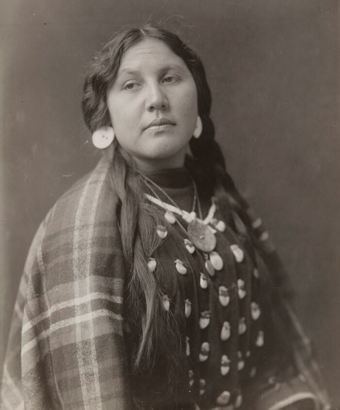 Vintage photograph of a Native American woman showcasing female strength in traditional attire with jewelry and braided hair.