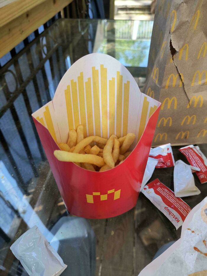 Small serving of fast food fries in a red container with sauce packets on a glass table showing product size changes.