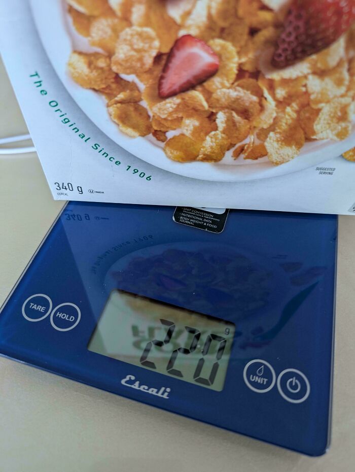Box of cereal weighed on a kitchen scale showing a smaller product size compared to original packaging weight.