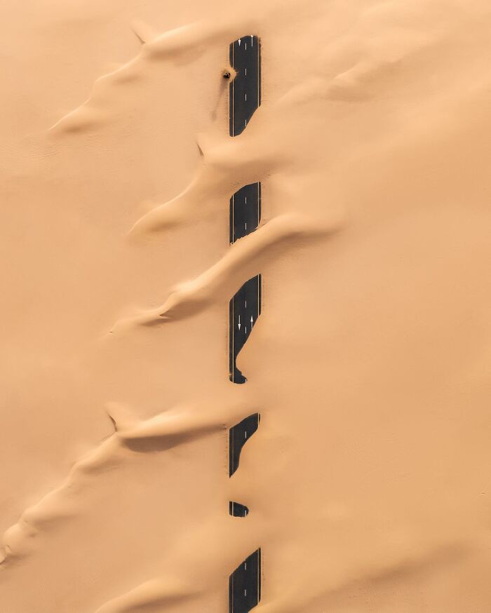 Aerial photo showing a desert road almost completely covered by sand dunes, illustrating stunning aerial photography.
