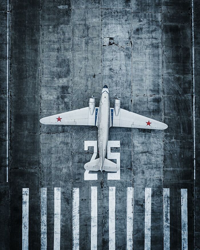Aerial photo of a vintage airplane with red stars on wings parked on a weathered runway marked with number 25