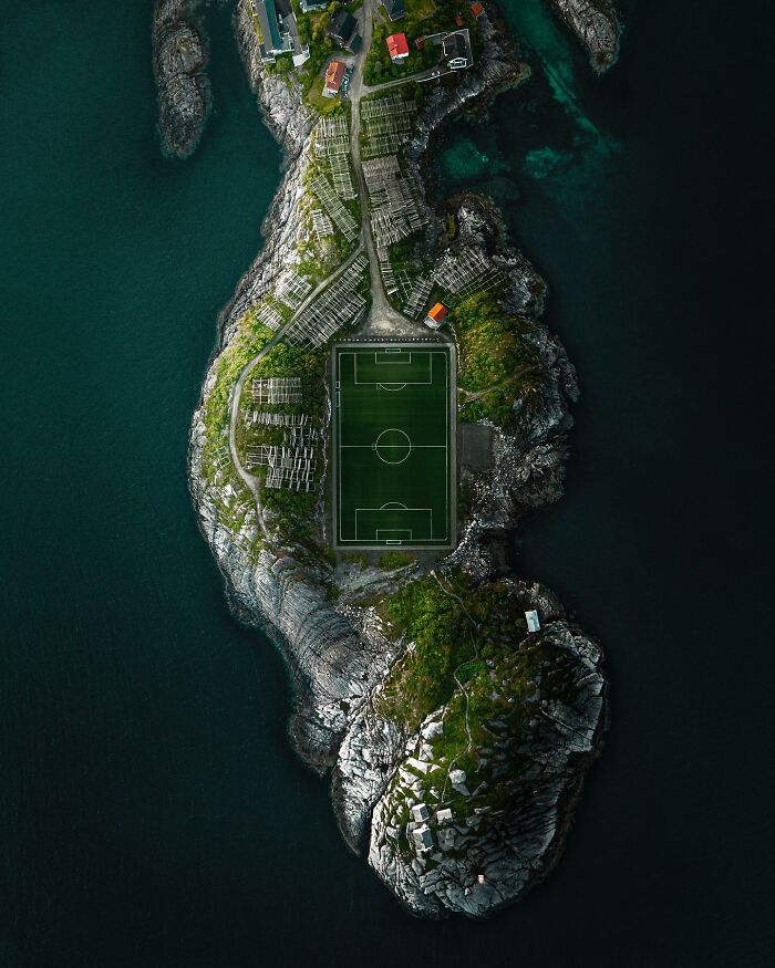Aerial photo of a secluded football field on a rocky island surrounded by dark blue ocean waters and sparse buildings.