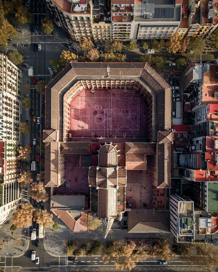 Aerial photo of a cityscape showing a large building with a basketball court in the center surrounded by streets and trees.