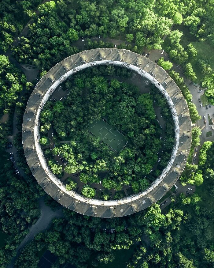 Aerial photo of a circular building surrounding dense greenery with a soccer field in the center, showcasing stunning aerial views.