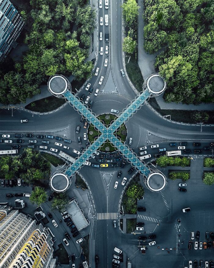 Aerial photo of a unique roundabout with glass pedestrian bridges crossing over busy roads surrounded by green trees and buildings.