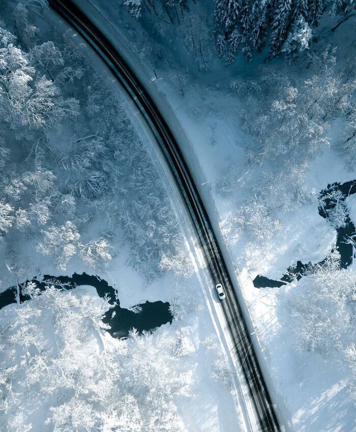 Aerial view of a snowy winter landscape with a winding road and a car, showcasing stunning aerial photos by Borsch.