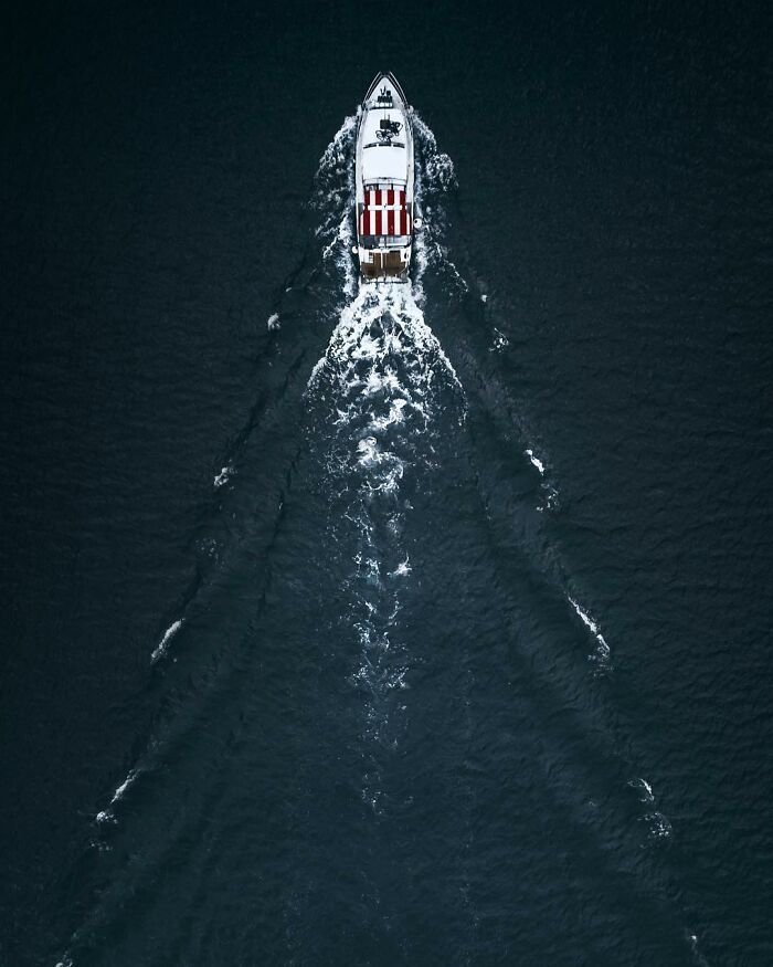 Aerial photo of a boat moving through dark water, creating white waves and patterns behind it.