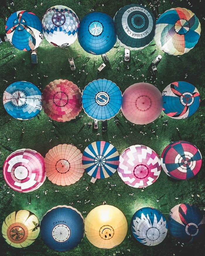 Aerial view of colorful hot air balloons arranged on green grass, showcasing stunning aerial photos from above.