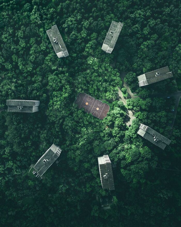 Aerial photo of a basketball court surrounded by dense trees and seven buildings, showcasing stunning aerial photography.