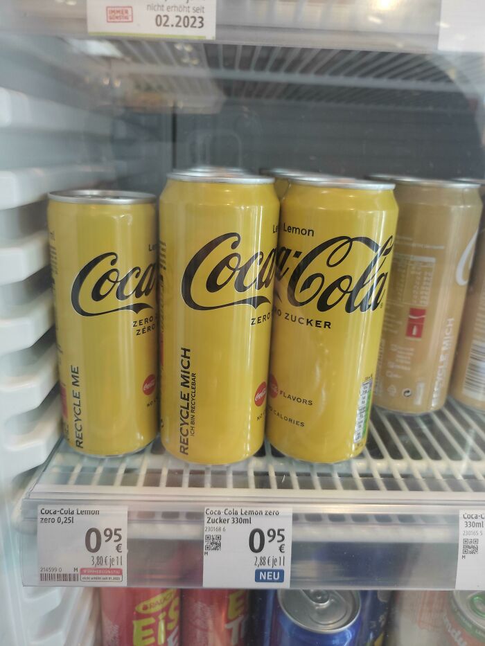 Yellow Coca-Cola lemon zero cans in a fridge showing small product sizes with higher prices on display.