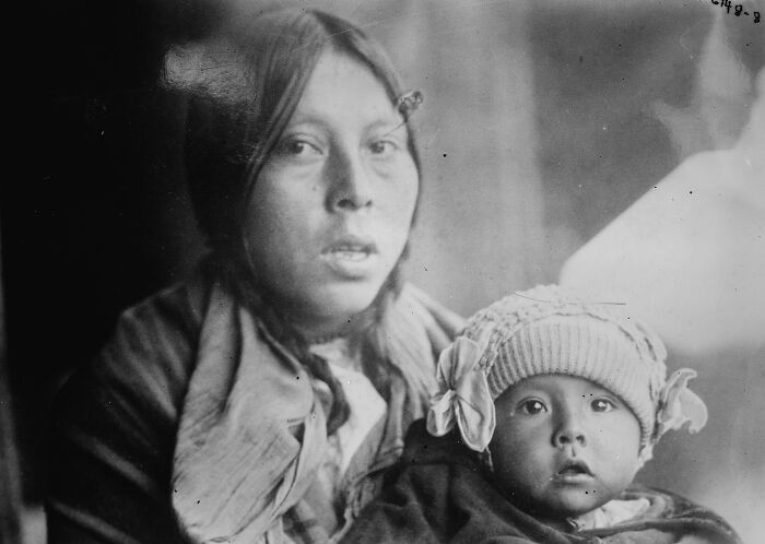 Native American woman holding child in a time-weathered black and white photograph showing female strength.