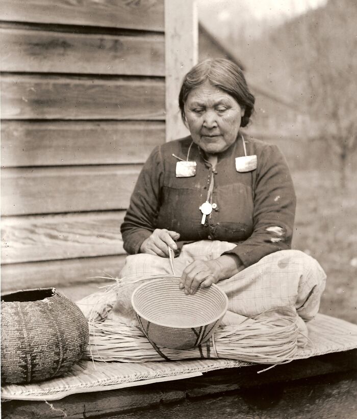 Native American woman weaving a basket, showcasing time-weathered strength and traditional craftsmanship outdoors.