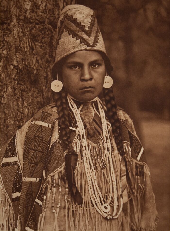 Native American female dressed in traditional attire with braided hair, honoring strength in a time-weathered photograph.