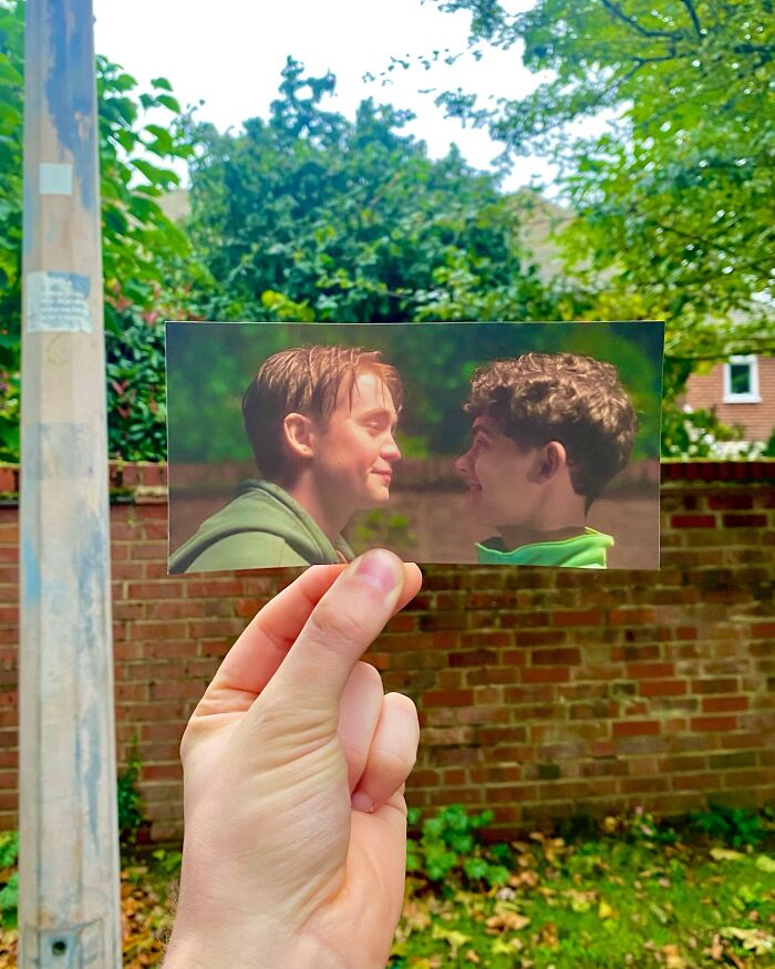 Hand holding a movie scene photo with two young men facing each other, showing real-life filming locations comparison.