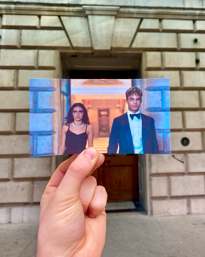 Hand holding a photo showing actors in formal wear at a real-life filming location of a movie scene.