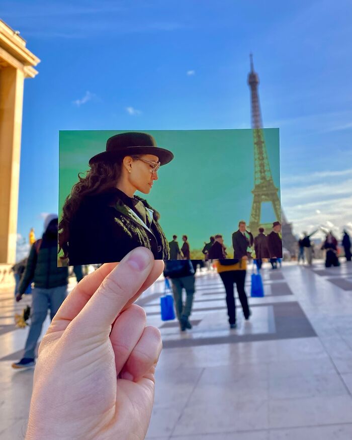 Hand holding a movie scene photo in front of the real-life filming location with the Eiffel Tower in the background.
