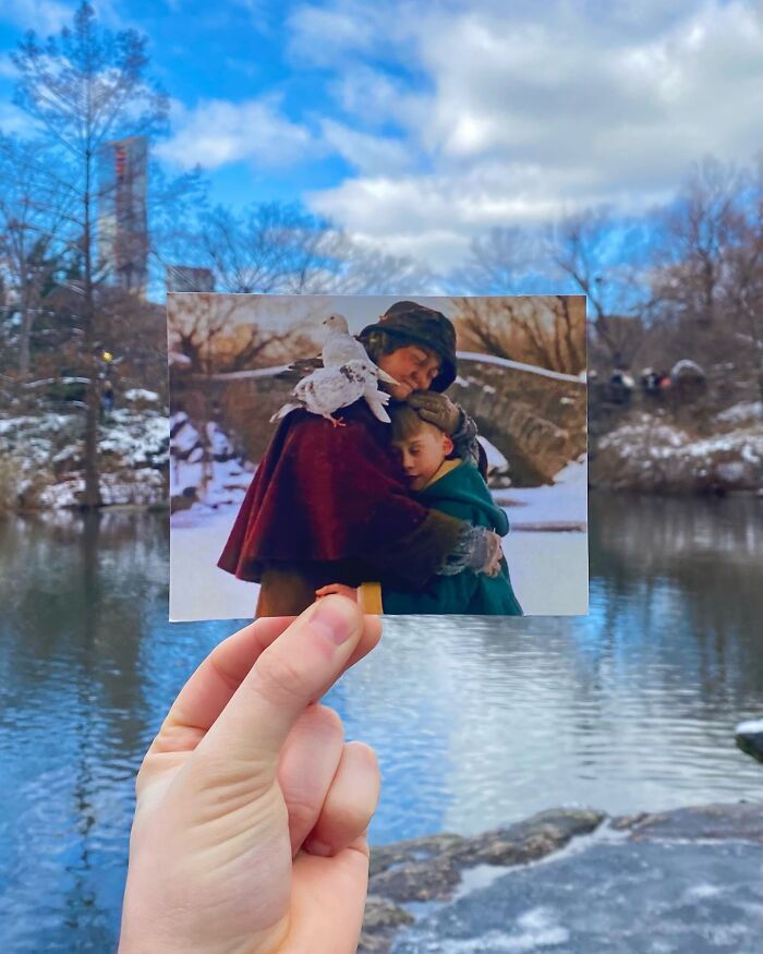 Hand holding a movie scene photo aligned with real-life filming location featuring snowy park and stone bridge.