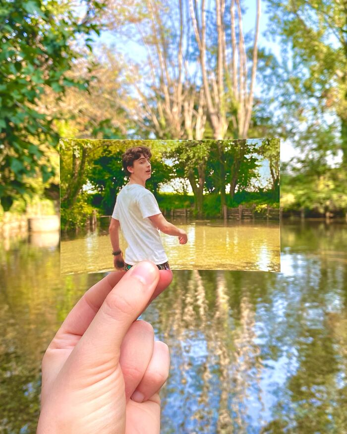 Hand holding photo of a movie scene with a young man by a river, showing a real-life filming location comparison.