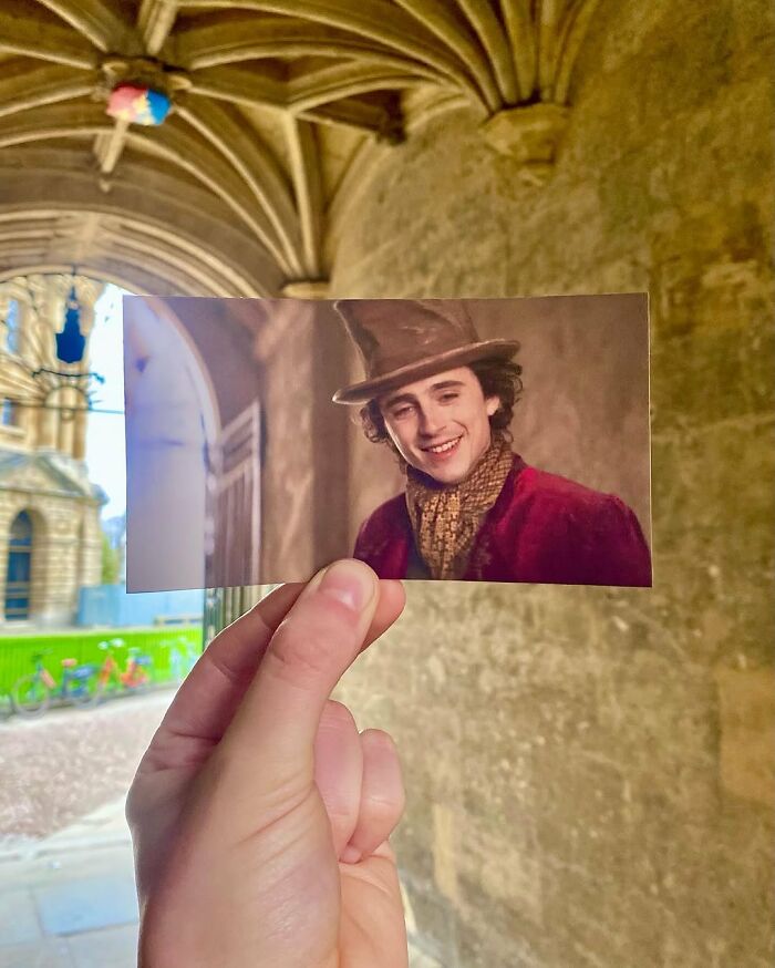 Hand holding a movie scene photo aligned with real-life filming location featuring an actor in period costume.