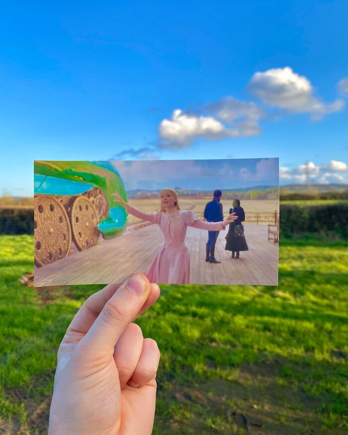Hand holding a movie scene photo aligned with real-life filming location under a clear blue sky, showcasing filming locations.