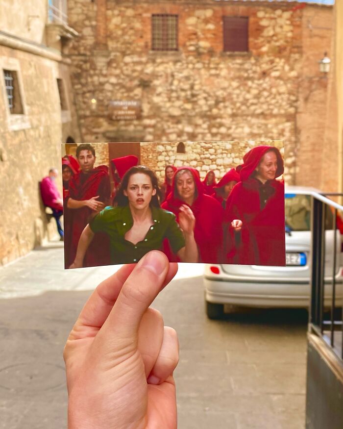Hand holding a movie scene photo in front of the same real-life filming location of a TV show scene outdoors.