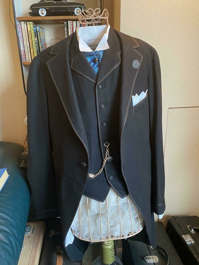 Vintage men's formal black suit with waistcoat and pocket watch chain displayed on an old-fashioned dress form, showcasing how things used to look.