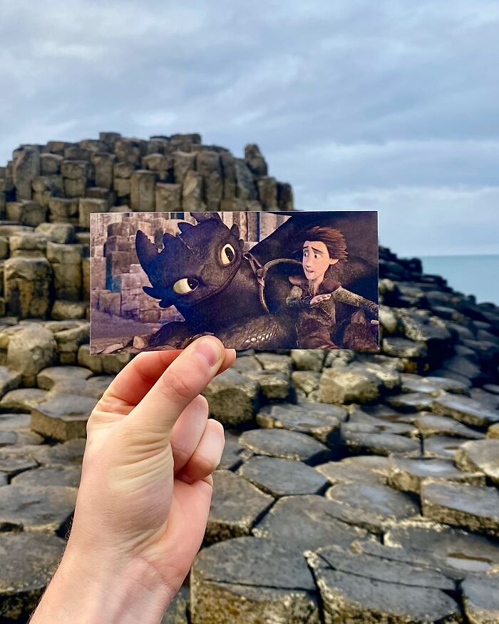 Hand holding a movie scene photo of animated characters against the real-life filming location of basalt rock formations.