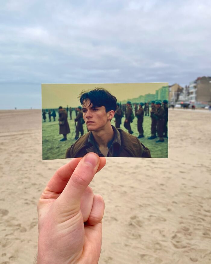 Hand holding a movie scene photo on a beach showing real-life filming location of war movie soldiers on sand.