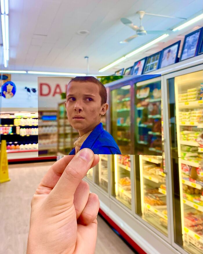 Hand holding a photo from a TV show scene inside the real-life filming location of a grocery store aisle.