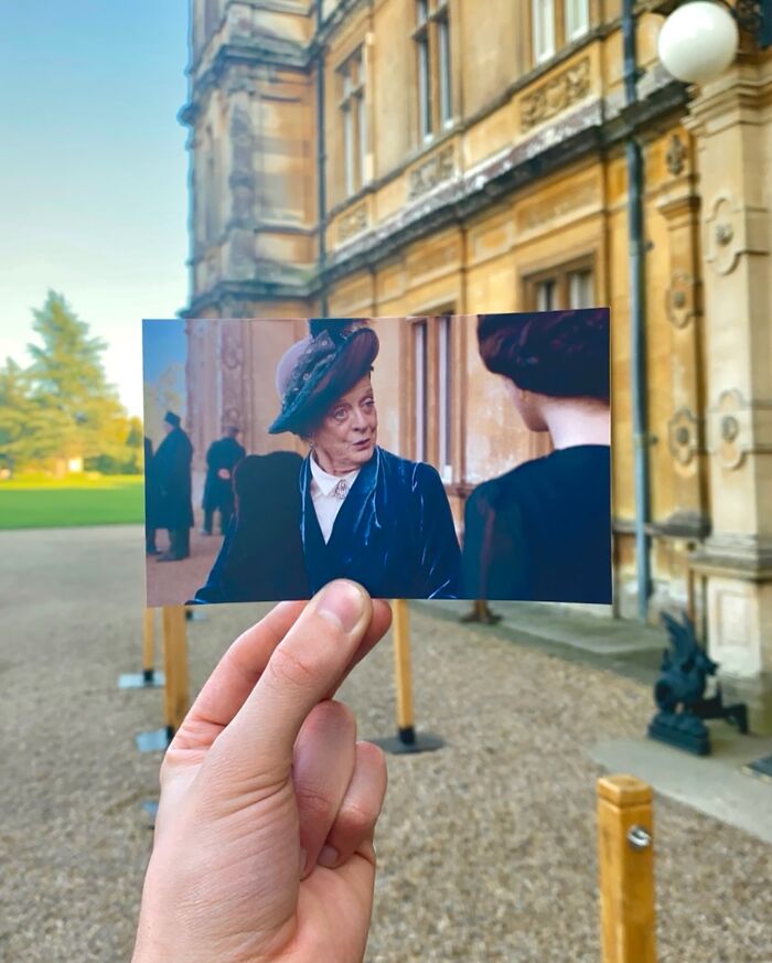 Hand holding a photo of a period TV show scene matched to the real-life filming location outdoors.