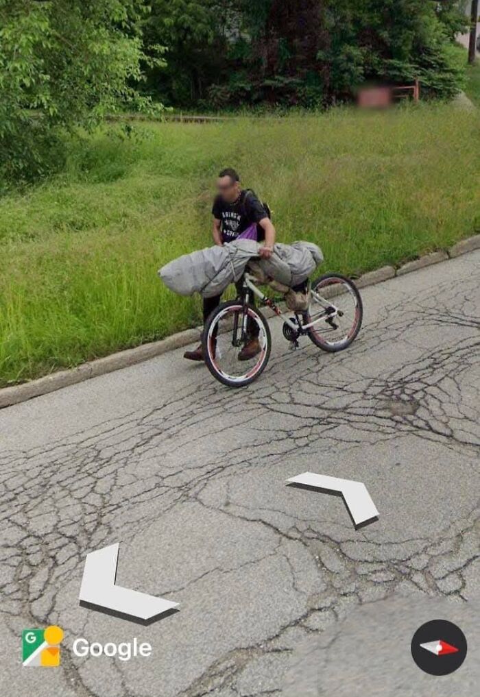 Person pushing a bicycle with an oddly shaped covered object along a c*****d road, found on Google Earth.