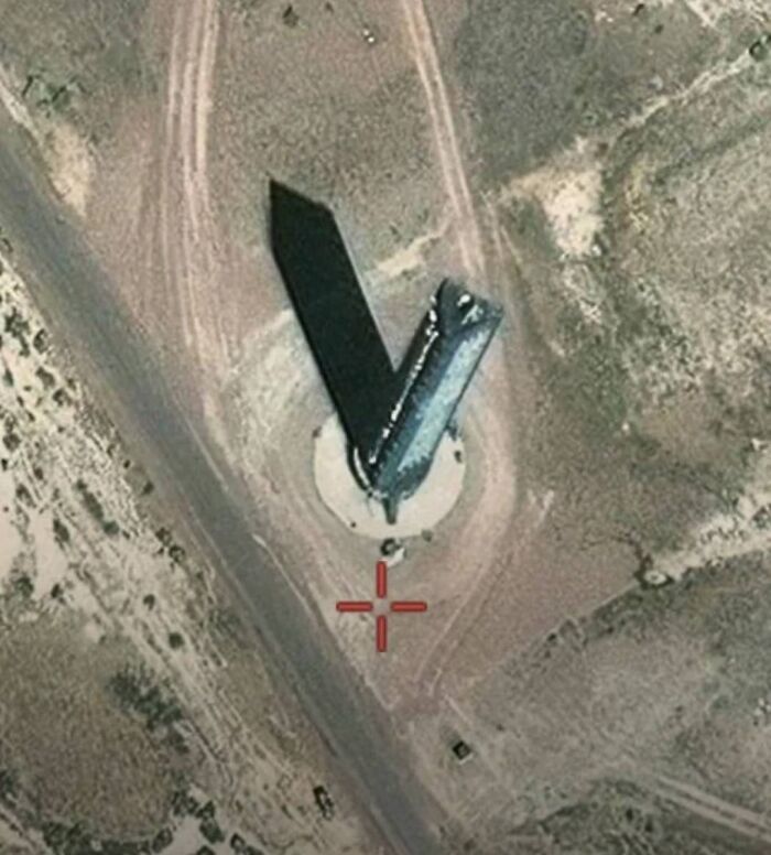 Aerial view of an unusual rocket-shaped structure casting a long shadow on barren land, found on Google Earth odd sightings.