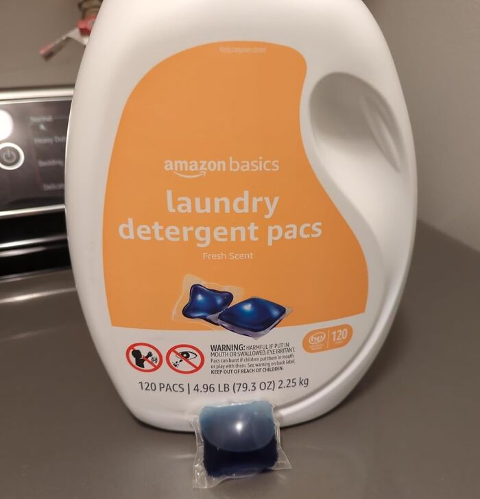 Amazon Basics laundry detergent pacs container with fresh scent and single pac on surface near washing machine.