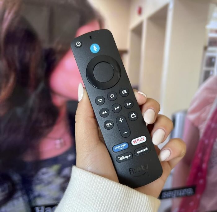 Hand holding an Amazon Fire TV remote with streaming app buttons during Amazon Memorial Day bargains shopping.
