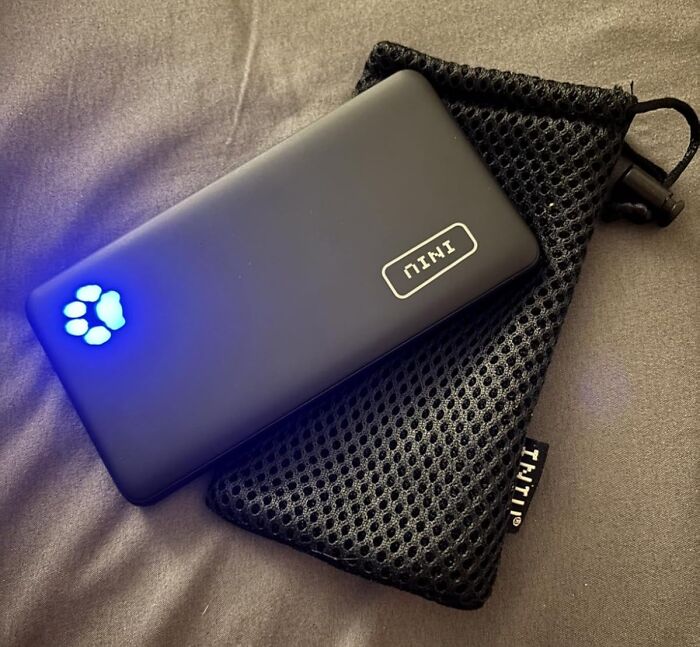 Portable black power bank with blue paw print light, resting on a black mesh pouch as an Amazon Memorial Day bargain item.