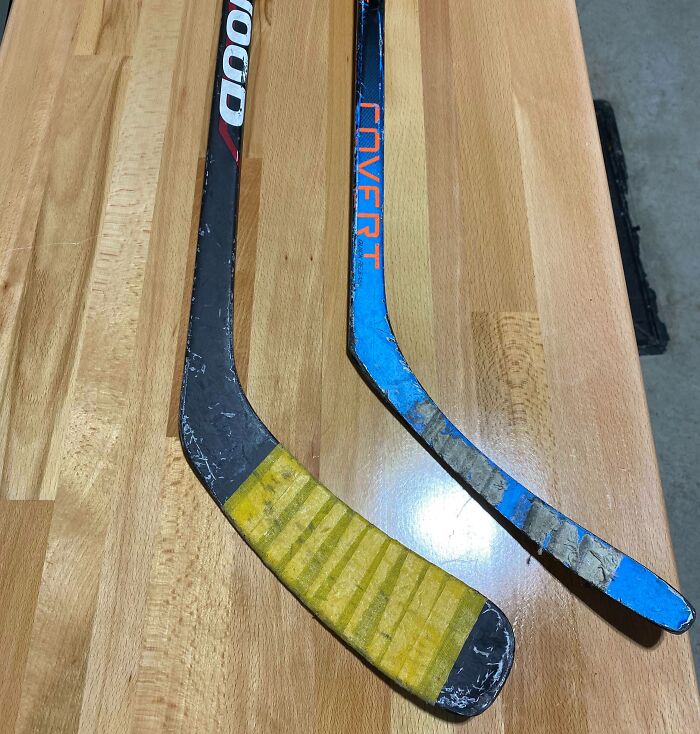 Two worn hockey sticks on a wooden surface showing before and after tape and wear, highlighting change over time.