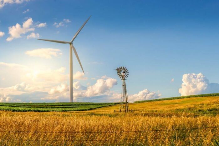 Modern wind turbine and old windmill in a rural field showing before and after photos of energy evolution.