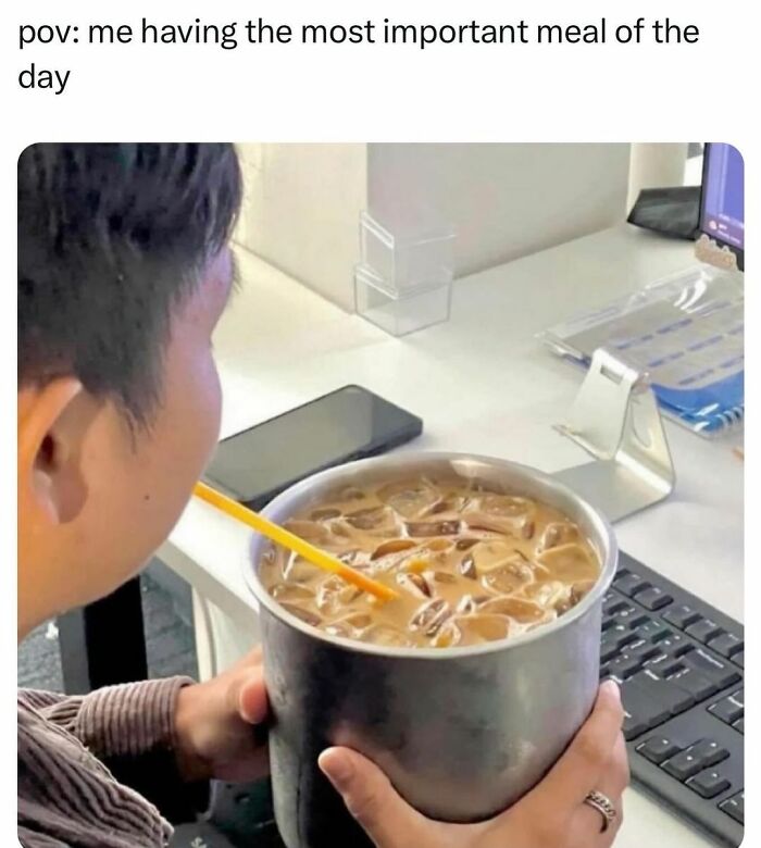 Person at desk holding an oversized cup of iced coffee with a straw, humorously showing barely holding it together.