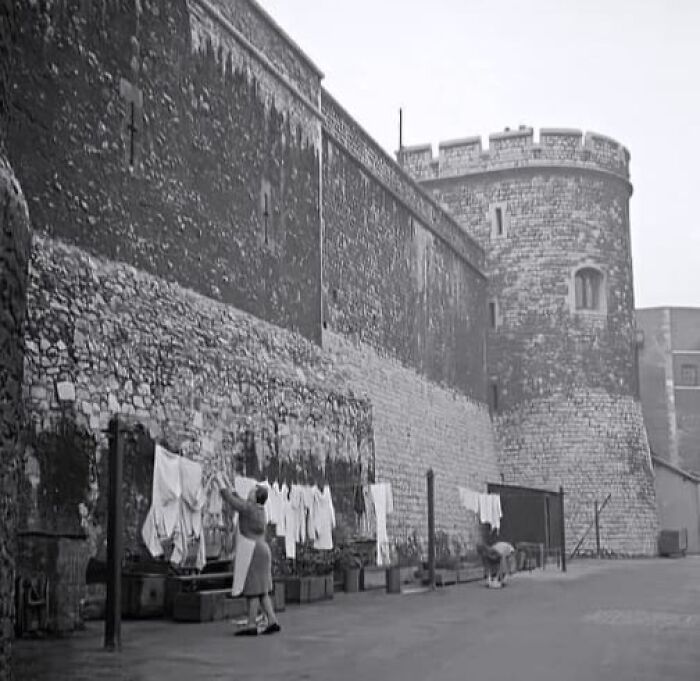 Women hanging laundry outside a stone fortress wall in an antique historical photograph showing daily life in the past.