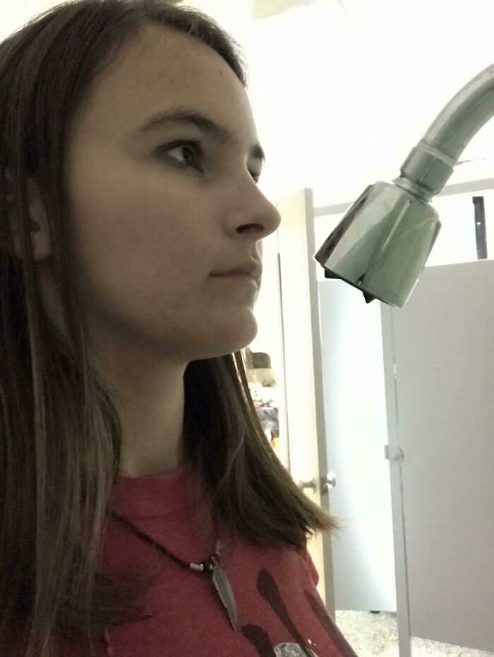 Woman standing very close to a showerhead in a bathroom, illustrating a dumb interior design decision.