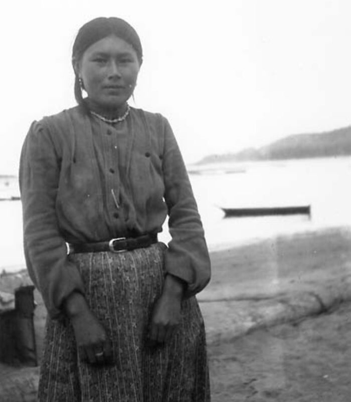 Native American woman standing near water in a time-weathered photograph honoring female strength and heritage.