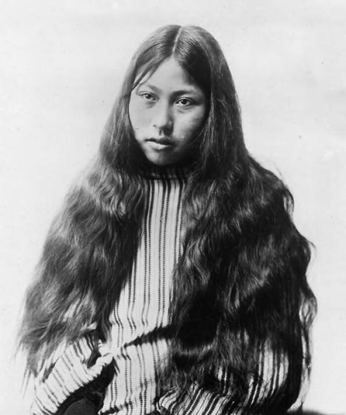 Vintage portrait of Native American female with long hair wearing traditional striped clothing, showcasing strength and resilience.