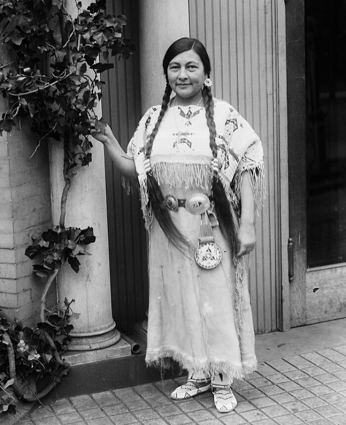 Native American woman dressed in traditional attire, showcasing female strength in a time-weathered black and white photograph.