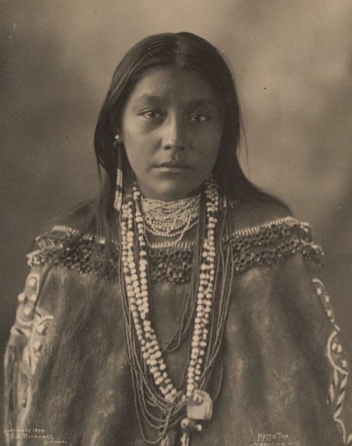 Native American woman in traditional attire and beadwork showcasing female strength in a time-weathered historic photograph.