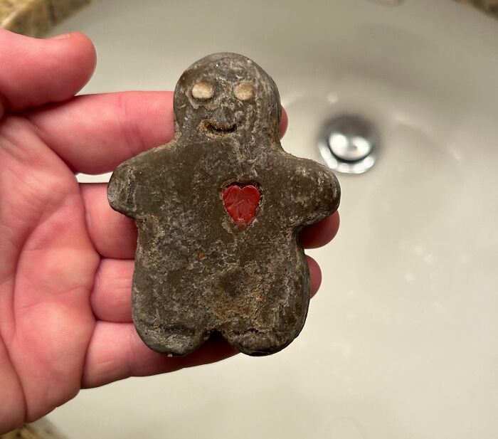 Hand holding a bizarre old gingerbread man figurine with a heart-shaped hole found in an old house.
