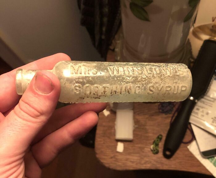Hand holding an old vintage bottle labeled Mrs. Winslow’s Soothing Syrup, a bizarre find in an old house.