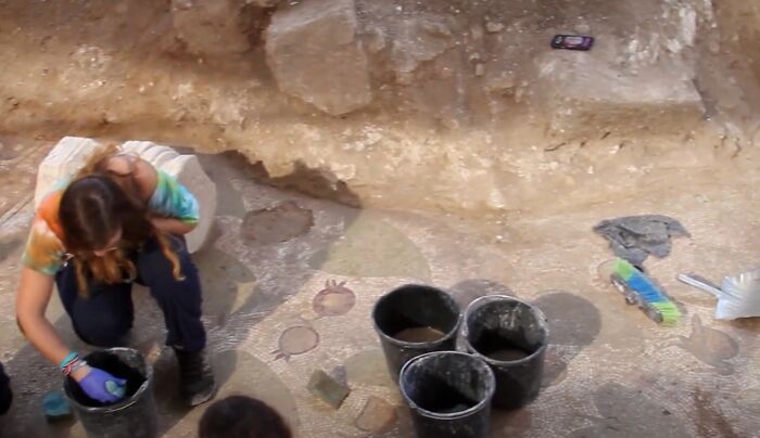 Archaeologist carefully excavating bizarre historical artifacts at an ancient dig site with buckets and tools nearby.