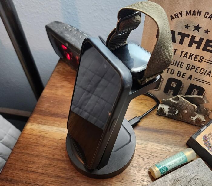Wireless charging stand on a wooden table holding a smartphone and a smartwatch during the Amazon Memorial Day Sale.