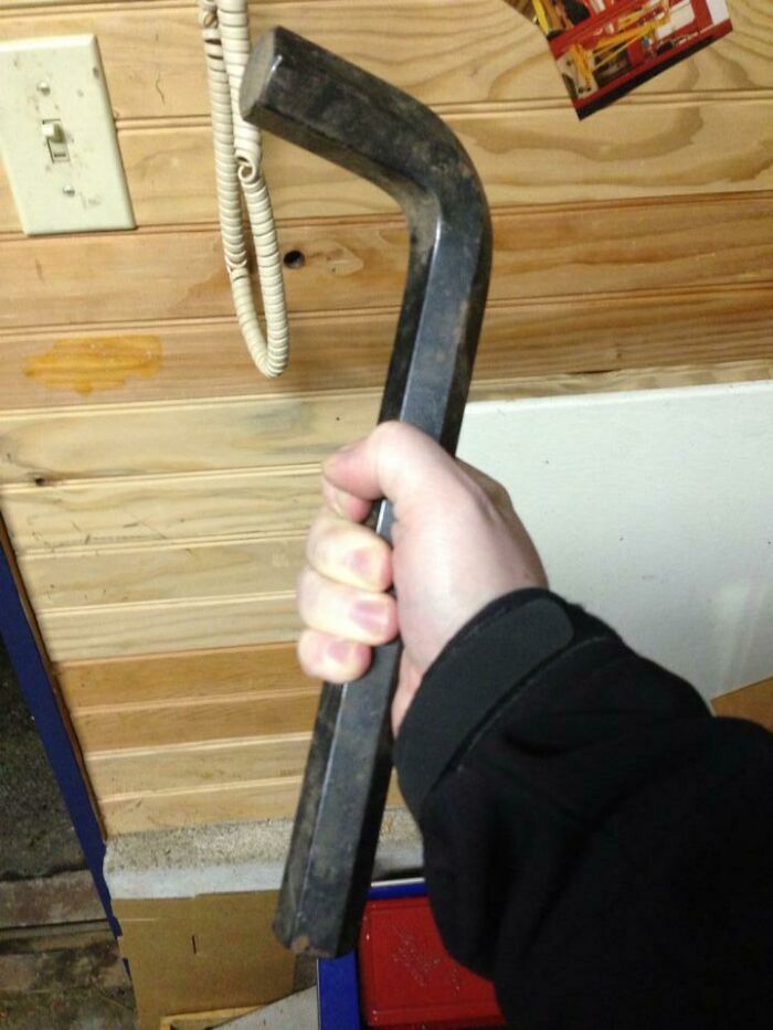 Hand holding a large hex key wrench indoors against a wooden wall in fascinating pictures for curious minds.